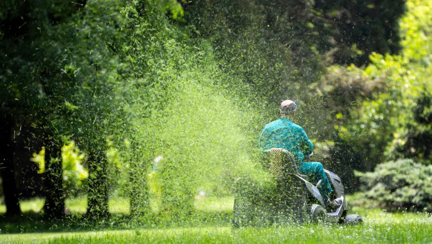 Man on a riding mower, spraying grass clippings.