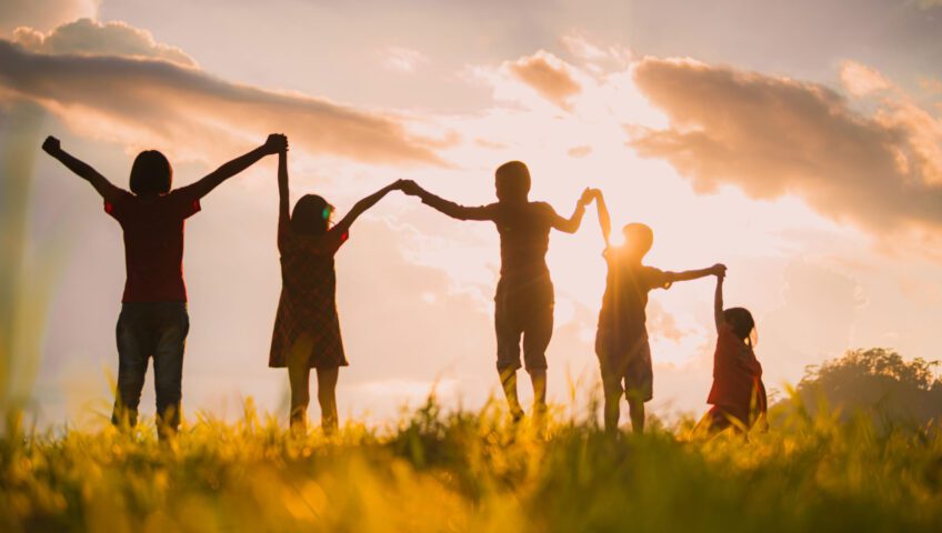 Kids holding hands in front of a sunrise