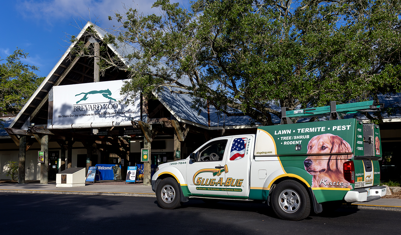 Brevard_Zoo_Web – Slug-A-Bug Pest Control – Slug-A-Bug Pest Control Entrance to Brevard Zoo with a large white banner sign and a service van parked at the curb outside on a sunny day